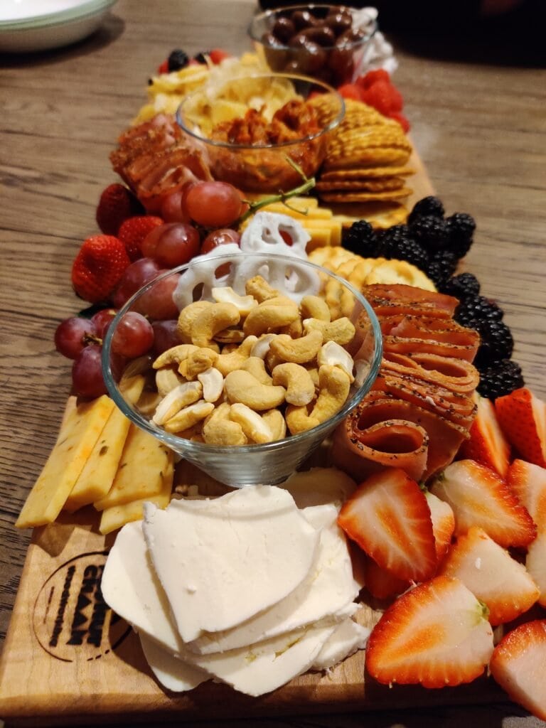 Koshur Chaan Woodworking Artisan walnut charcuterie board with cheeses, meats, fruit, and snacks displayed on a wood table; premium Georgia woodworking. Johns Creek, GA