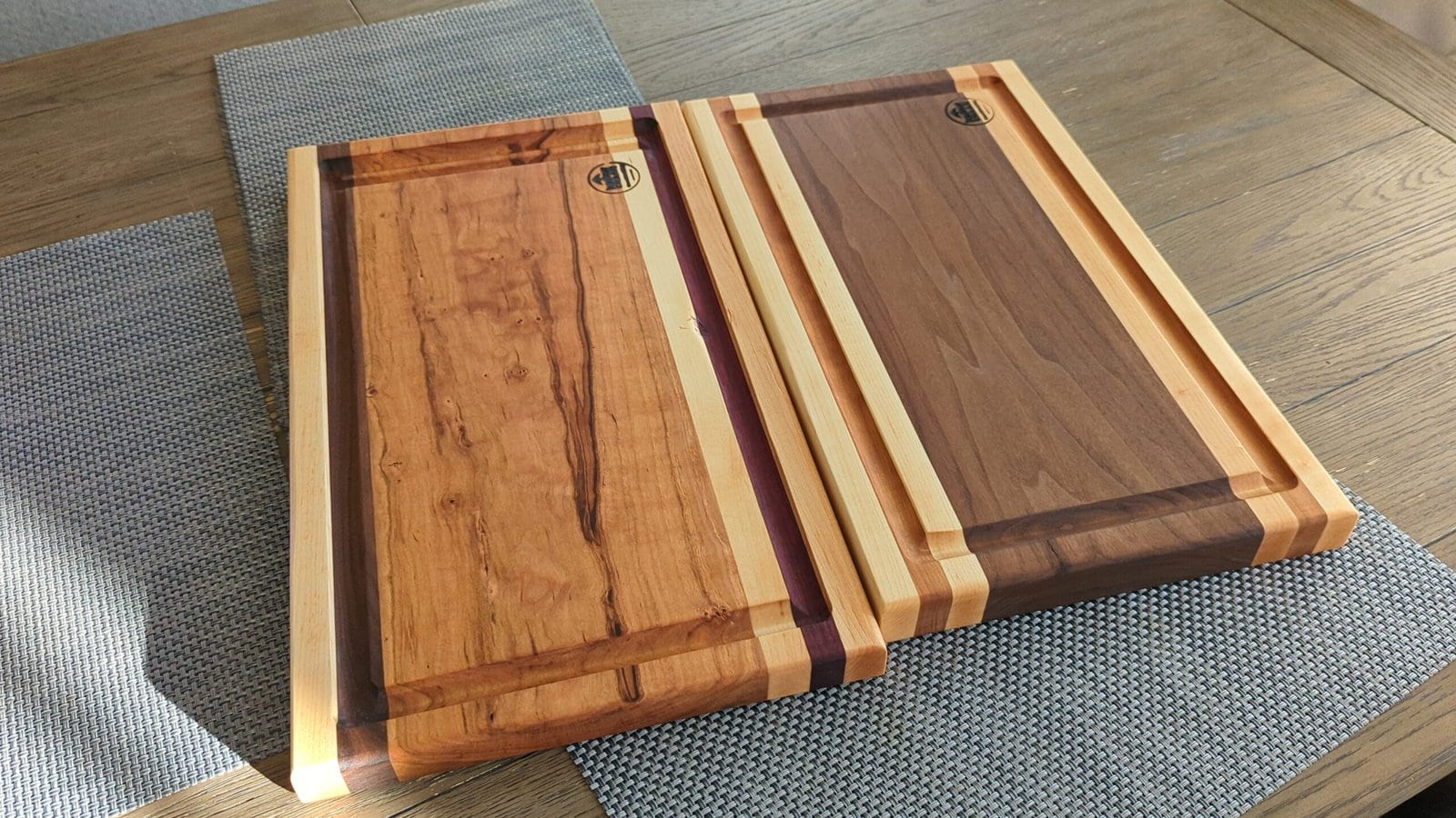 Two handmade edge-grain cutting boards with juice grooves, set on woven placemats