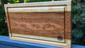 Hardwood cutting board with pale border and striped inlay displayed outdoors