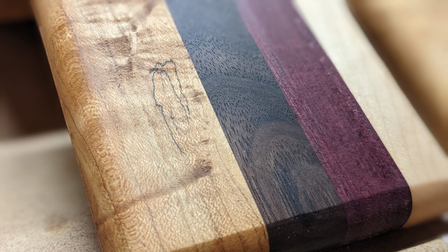 Close-up of a striped board with figured maple, walnut and a purple accent stripe