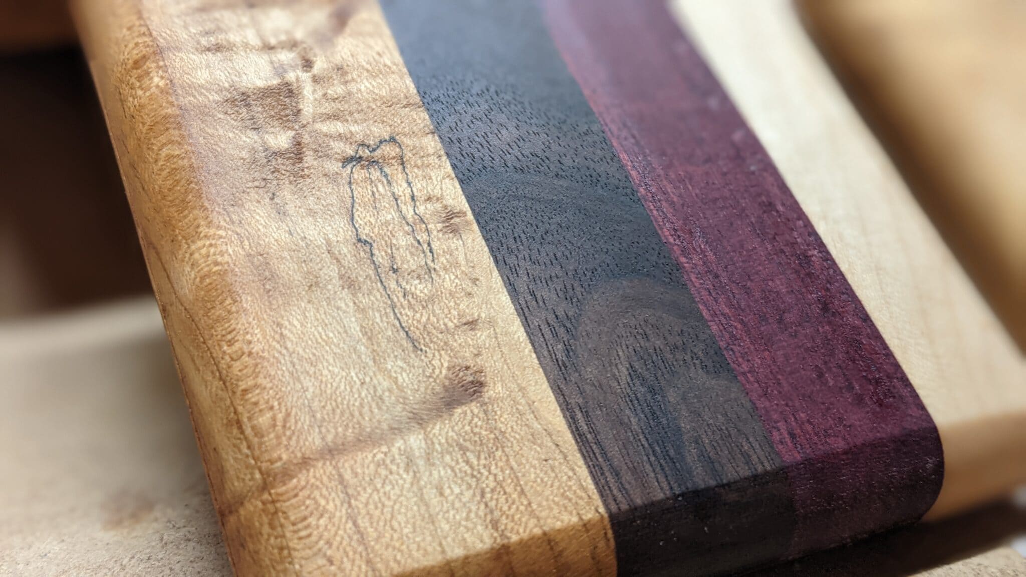Close-up of a striped board with figured maple, walnut and a purple accent stripe