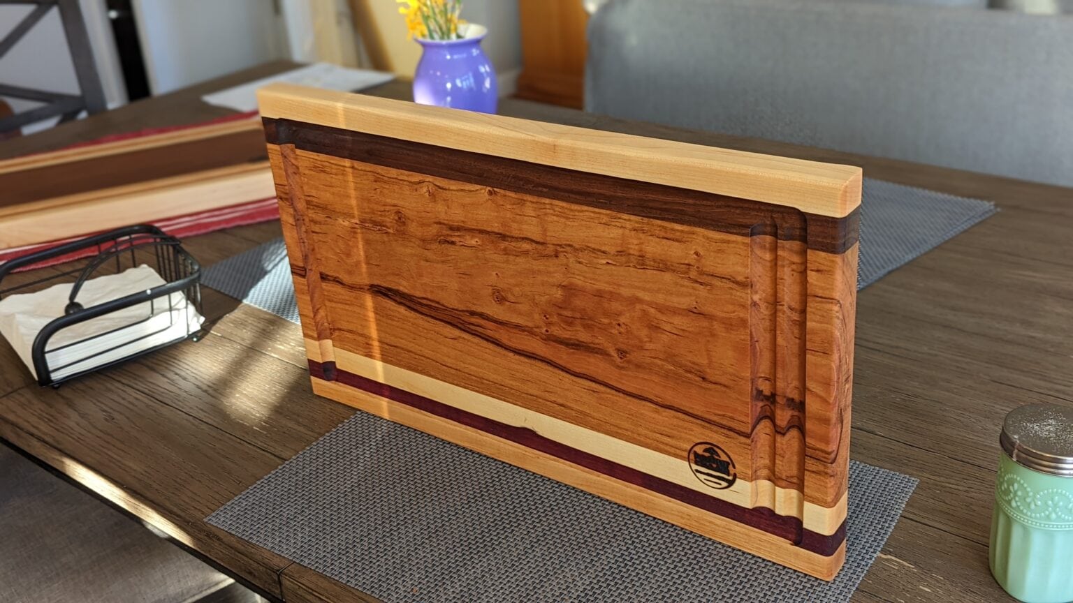 One of my cutting boards in Johns Creek: figured hardwood cutting board with walnut accents and a juice groove, standing on a table
