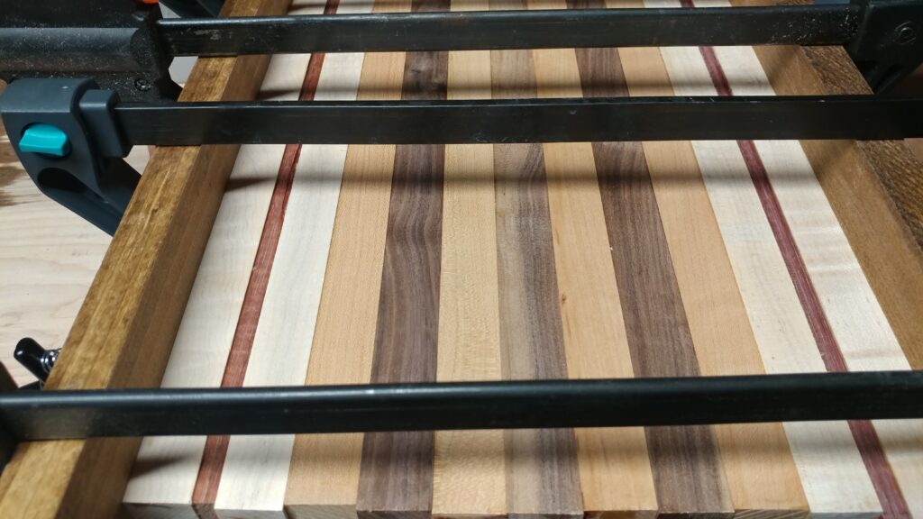 Cutting boards in Johns Creek start here: a striped board held flat under black bar clamps in the workshop