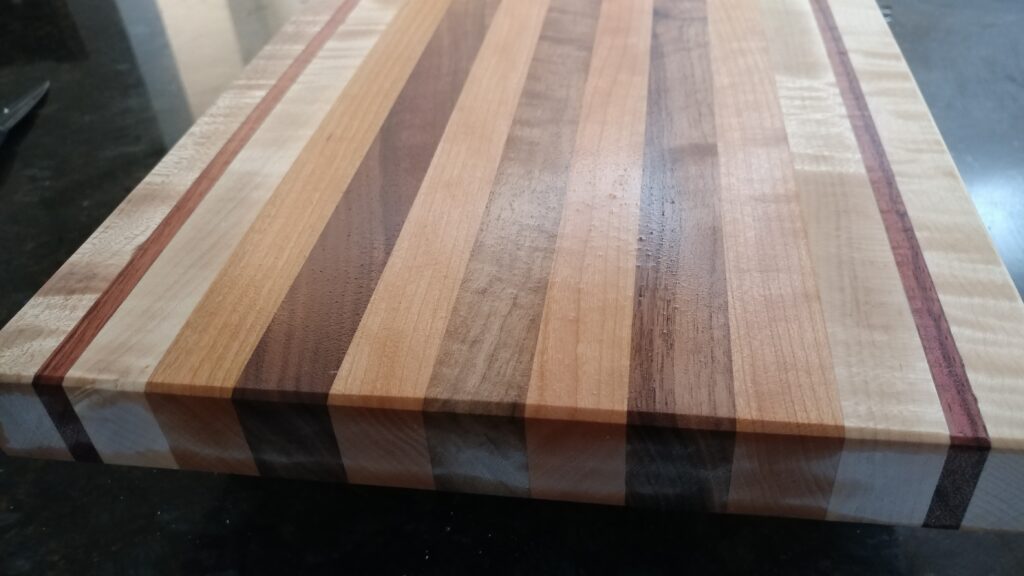 How to care for a wood cutting board: a smooth striped board with alternating pale, brown and reddish hardwood strips