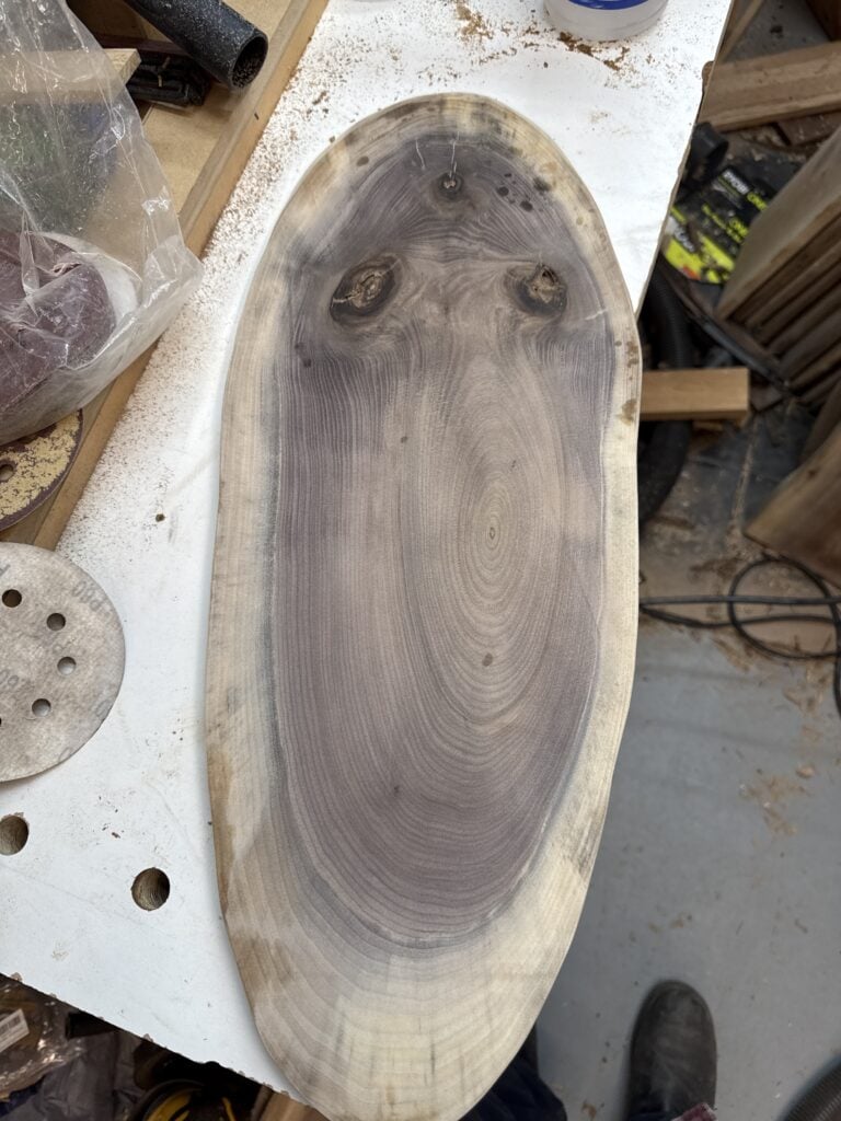 From the woodworking journal: close view of an oval wood slab with swirling dark grain, three knots and a pale outer edge