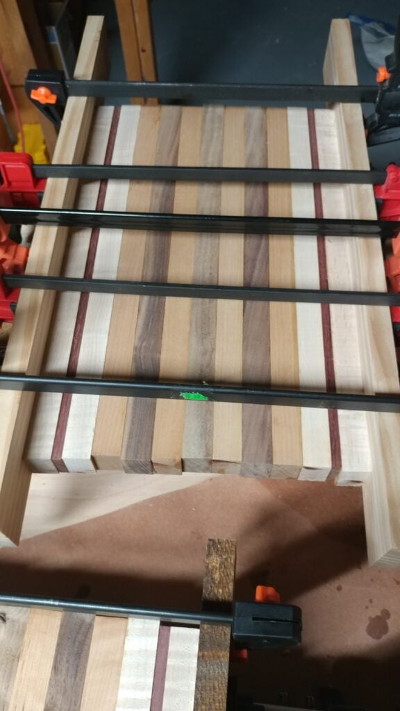 Light and brown wood strips with red accents glued up under black bar clamps