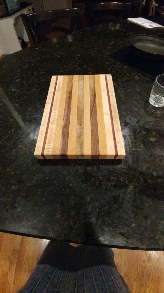Striped cutting board with light, brown and narrow red stripes resting on a dark kitchen counter
